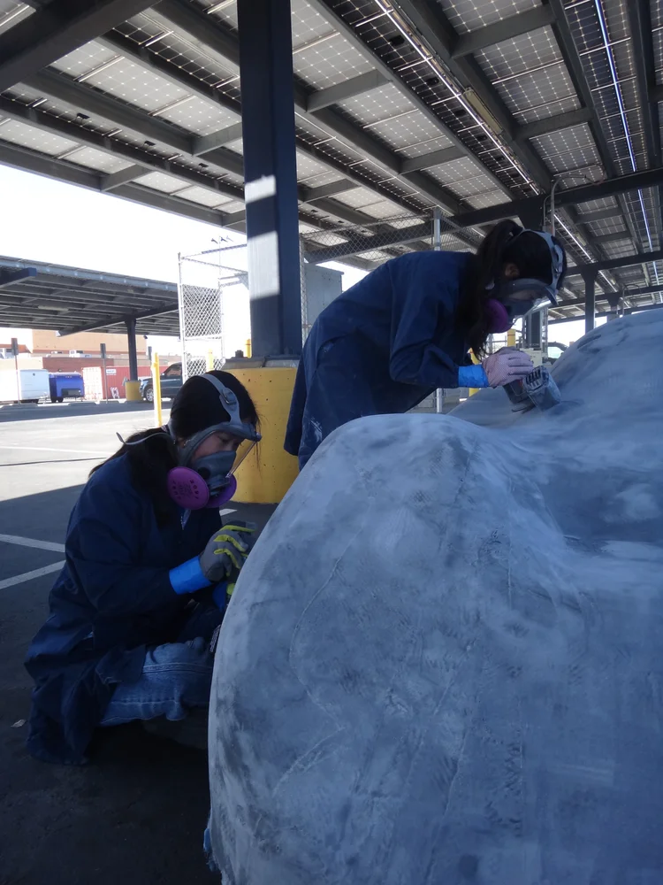 Team members in protective gear sanding the mold